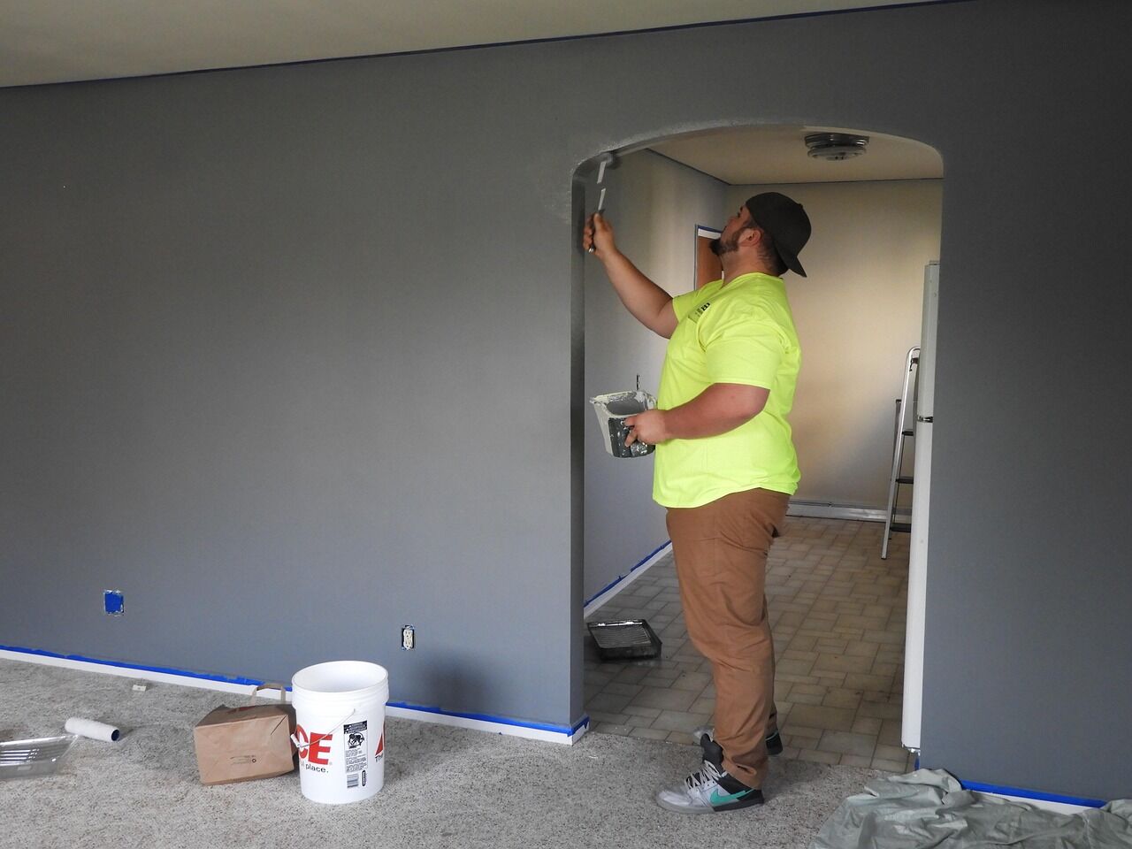 Painter using a brush on a gray wall next to an archway