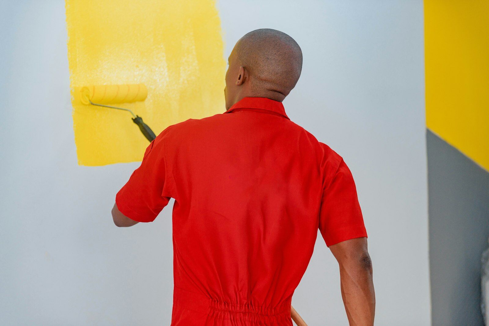 Painter using a roller to apply yellow paint to a white wall