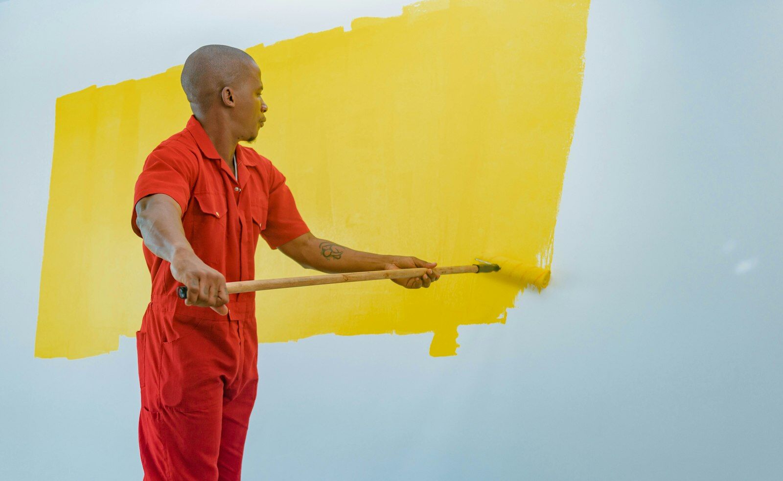 Painter using an extension roller to cover a white wall with yellow paint