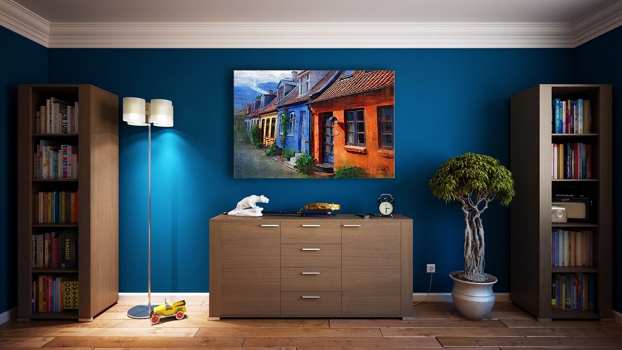 Living room with a deep blue wall, a wooden cabinet, and a painting of colorful houses